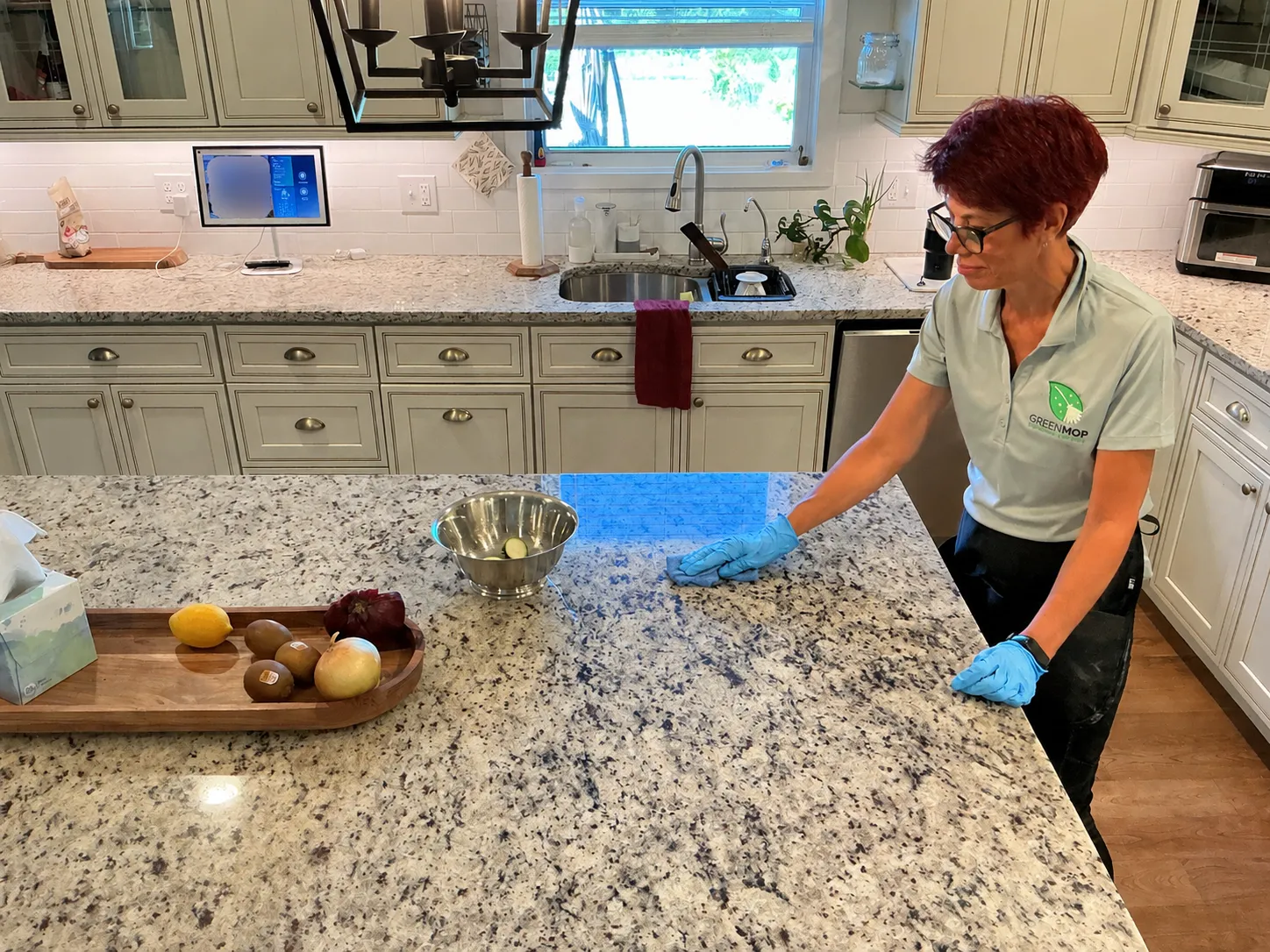 A Green Mop cleaner in a Green Mop polo wiping a granite kitchen island with a blue cloth